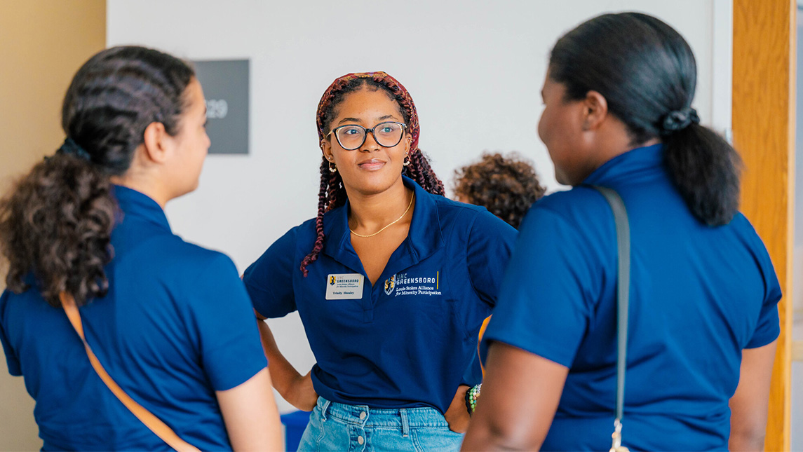 A group of UNCG students stand in a hallway wearing matching t-shirts.