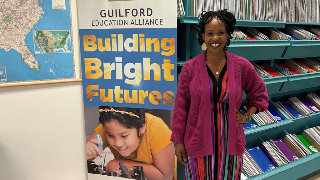 UNCG alumna Dr. Zithoble "Zitty" Nxumalo '11 stands beside a large banner for Guilford Education Alliance.