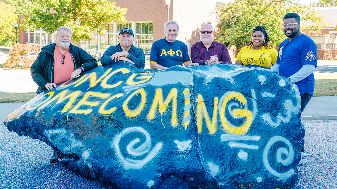 Five UNCG alumni gather around the Rawk painted for Homecoming.