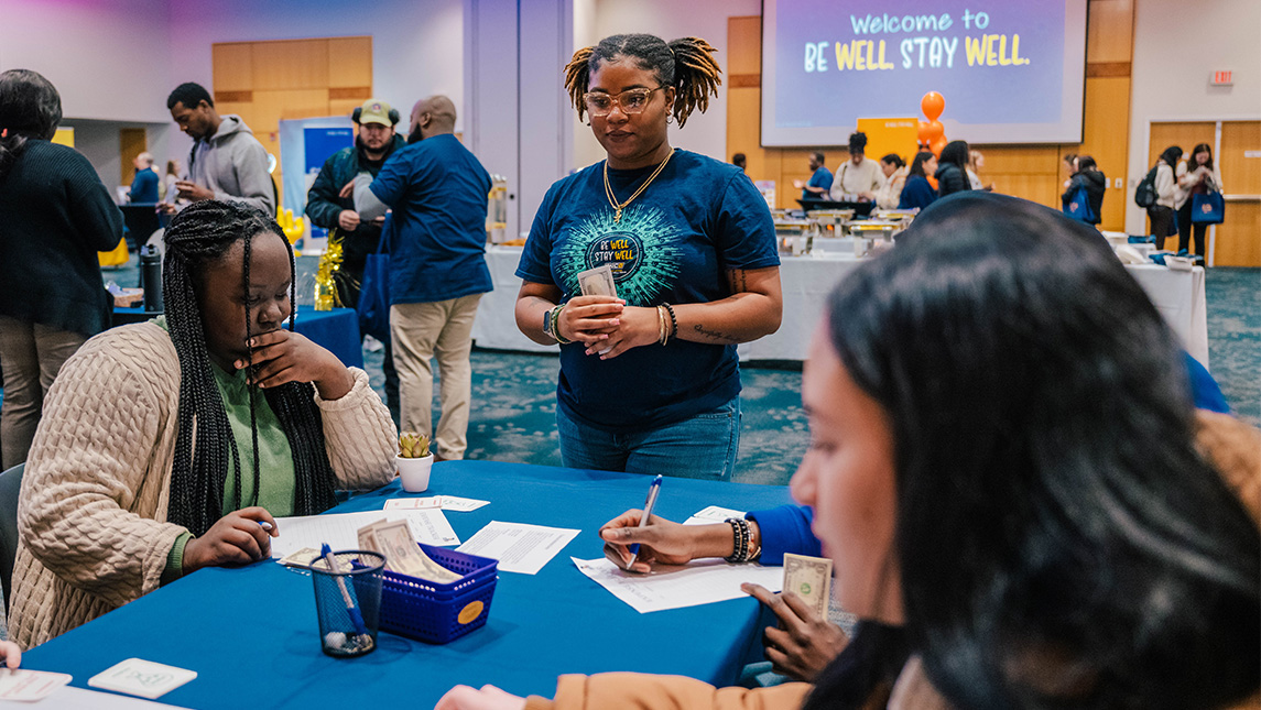 A UNCG student talks to other students sitting at a table and writing.