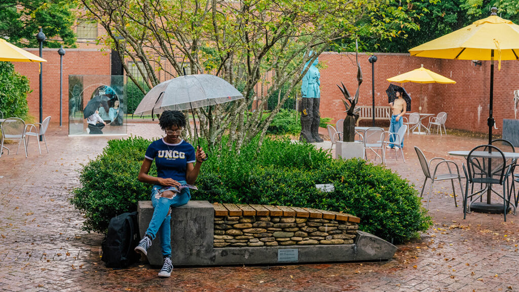 Students hold umbrellas in the rain of the Weatherspoon Courtyard.