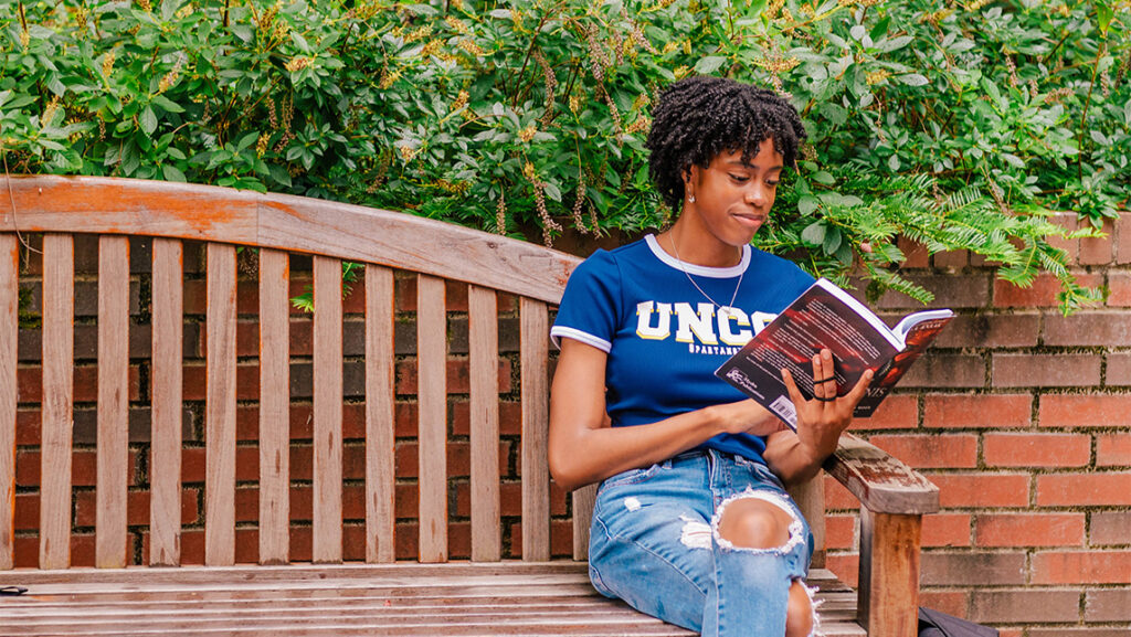 A UNCG student reads a book on a bench.