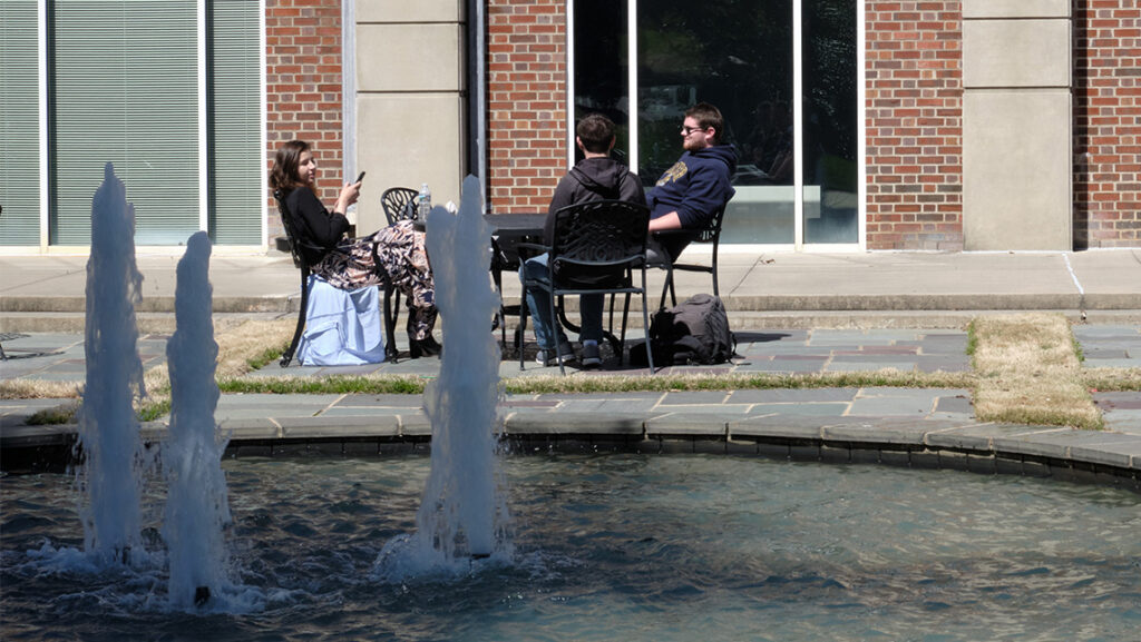 A group of UNCG students sit around a table beside a fountain.