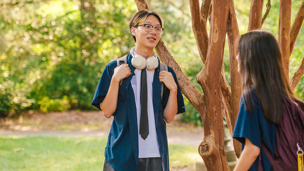 Students chat in the shade of a tree.