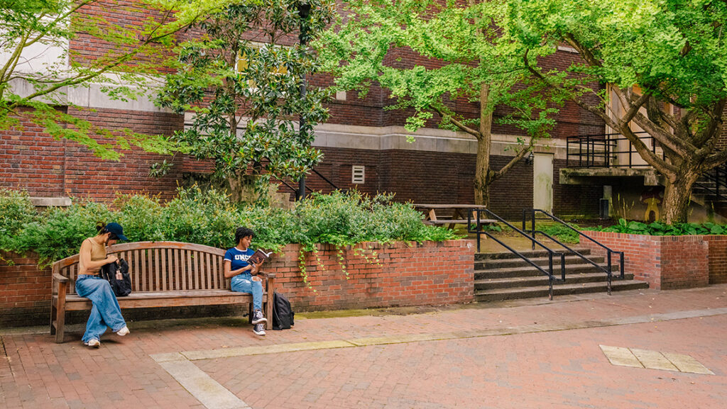 Students read and work on homework on a bench at UNCG.