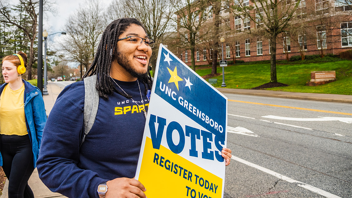 A UNCG student carries a sign encouraging people to vote.