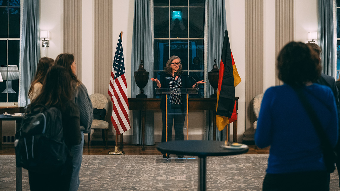 Speakers at UNCG's International Dialogues Exploring Partnerships reception address an audience between the American and German flags.