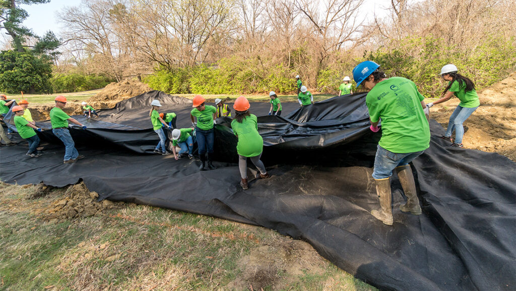 A team of people in hard hats roll out tarp at UNCG's Peabody Park.