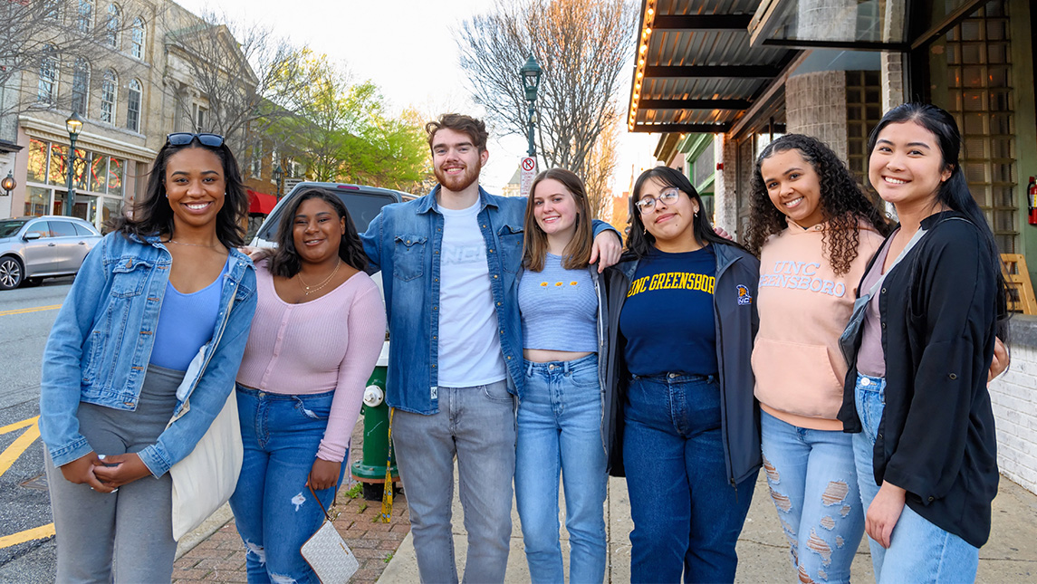 Six UNCG students put their arms around each other on Tate Street.