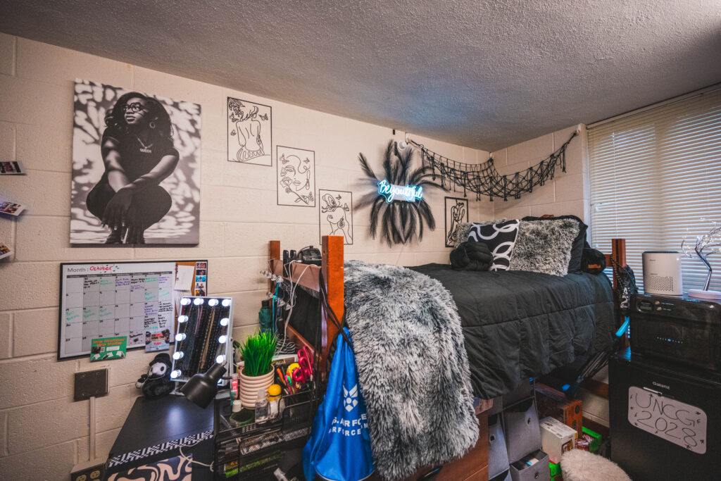 Dorm room decorated in black and grey with black and white artwork on the walls above a raised bed.