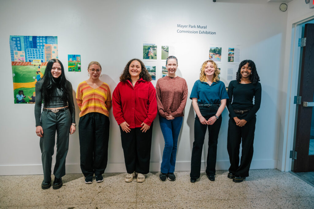 Six students stand together in front of an art gallery wall.