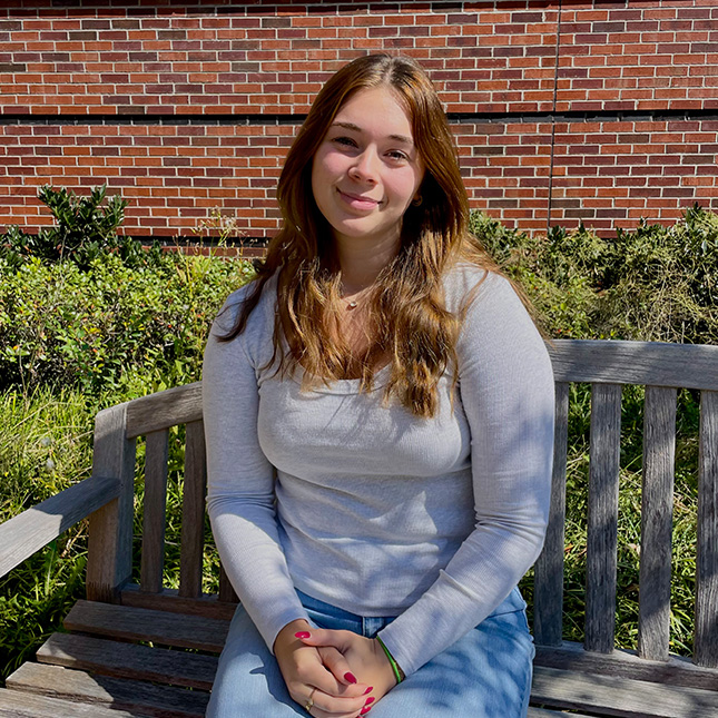 Student sits on a bench in front of a brick wall.