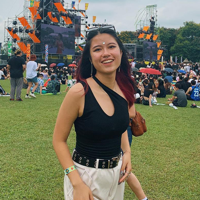 Girl poses in front of a stage at a music festival.