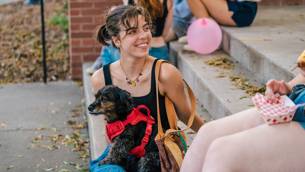 A UNCG student holds a small black dog while she chats on the steps with other students.