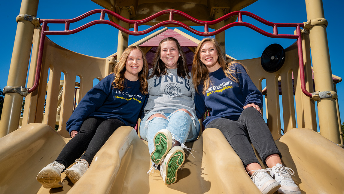 UNCG students Brooke parks, Mary Grace Smith, and Sidney Cassidy sit atop a slide.