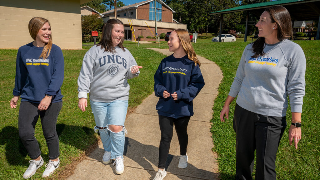 UNCG students walk with Professor Emily Hamuka in a park.