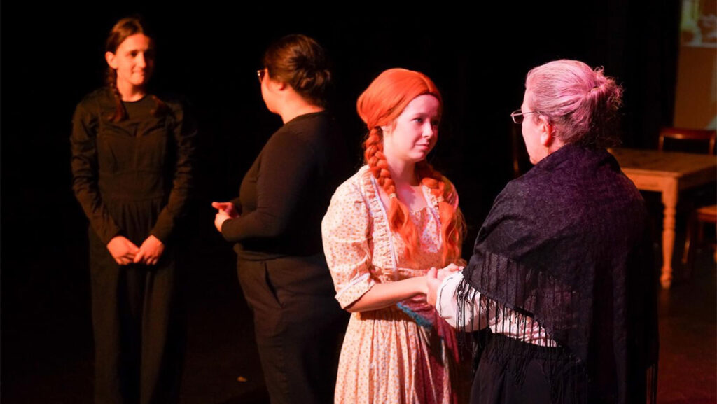 Actors in Anne of Green Gables talk to each other, while interpreters in black clothes mirror their interaction.