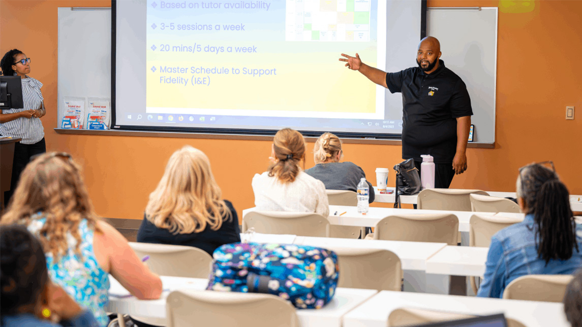 Students watch a man give a presentation about UNCG's tutoring program.