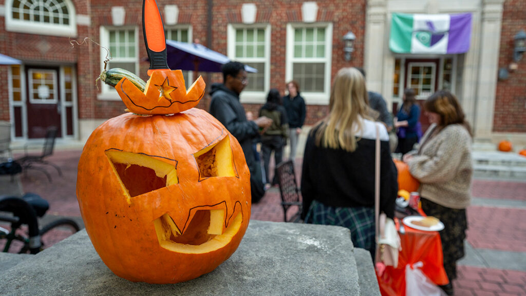 A jack-o-lantern with the carving knife sticking out of its head rests on a stoop.