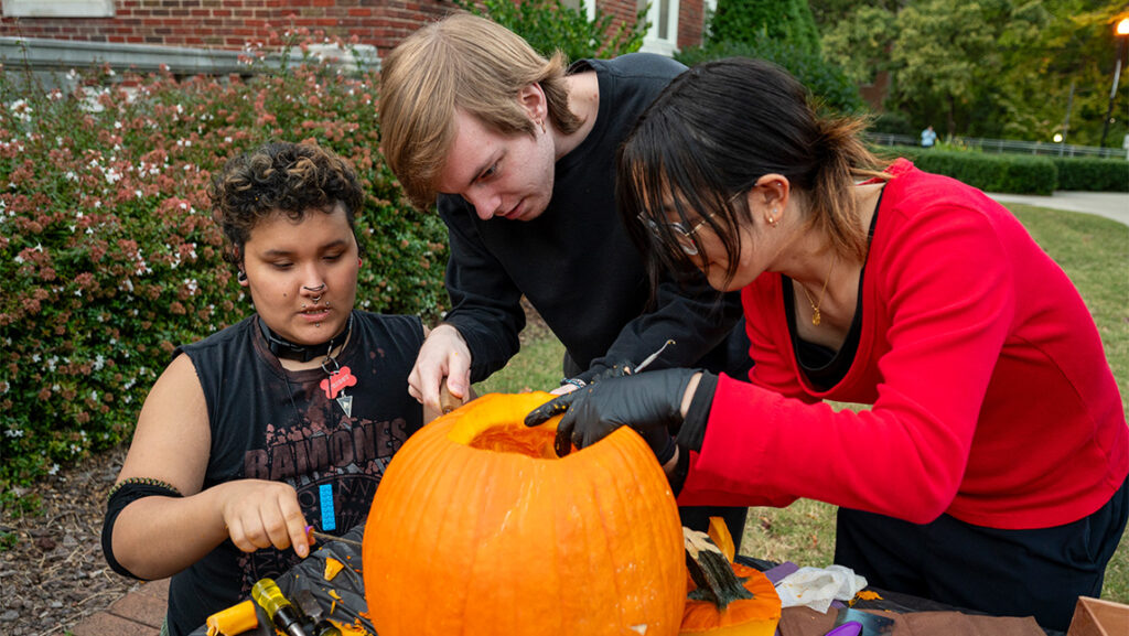 Three UNCG Residential College students carve into a pumpkin.