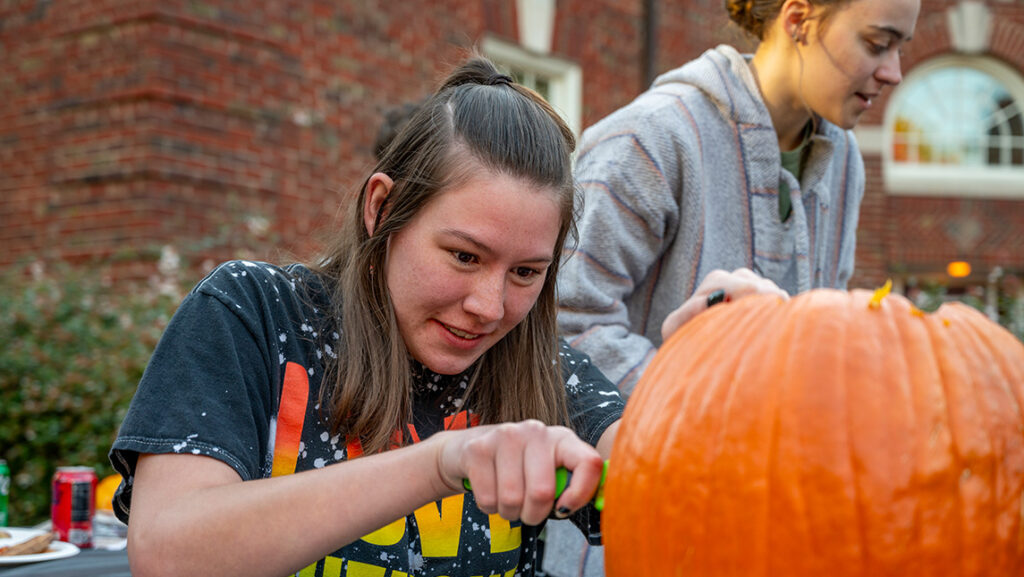 A UNCG Residential College student carves into a pumpkin.