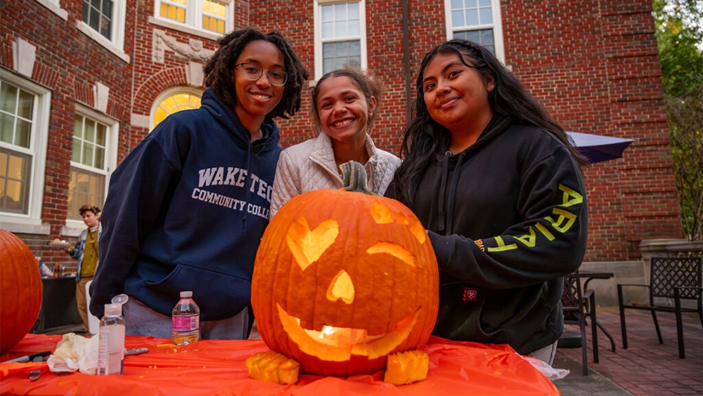 Three UNCG Residential College students smile behind their jack-o-lantern.