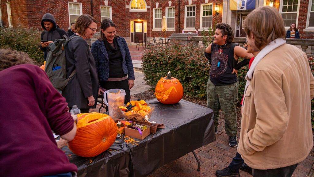 UNCG Residential College students show their carved pumpkins to a staffmember.