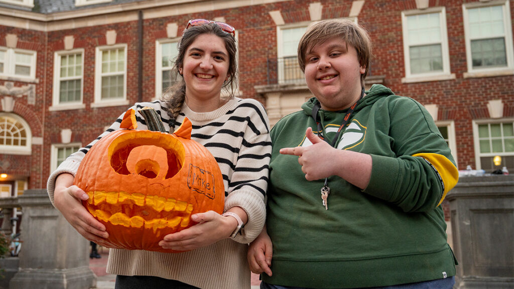 Two UNCG Residential College students point to their one-eyed jack-o-lantern.