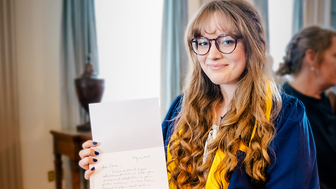 UNCG student Raven Sizemore '24 in her graduation gown holds up a congratulatory letter.