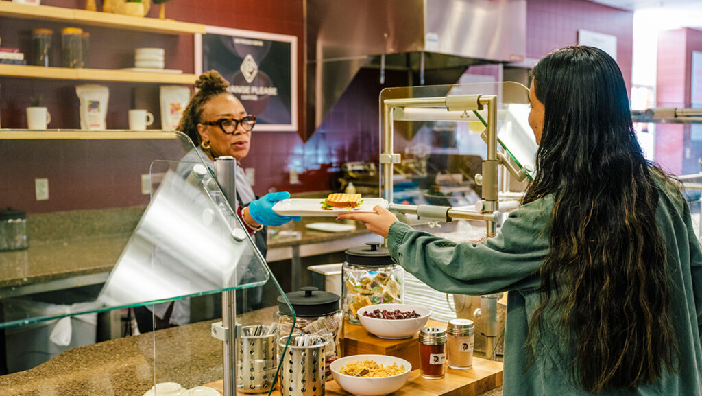 A worker for UNCG's coffee shop hands a plate with a sandwich to a student.