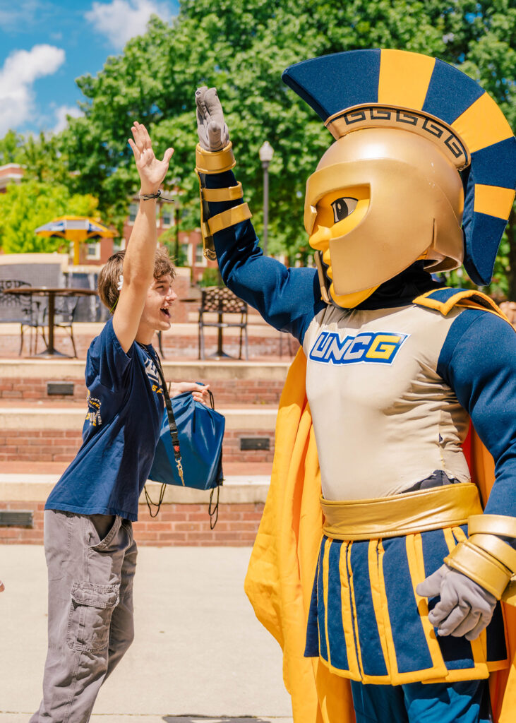 Student high fives Spiro in front of Moran Commons. 