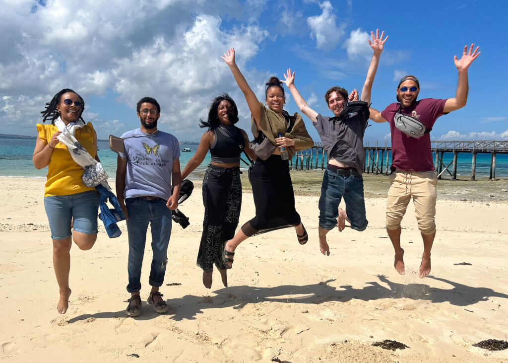 Study abroad students jump together on a beach in Tanzania.