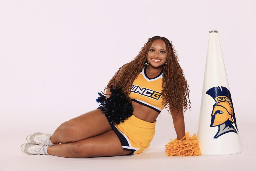 UNCG cheerleader poses seated on the floor with a Spartan megaphone beside her. 