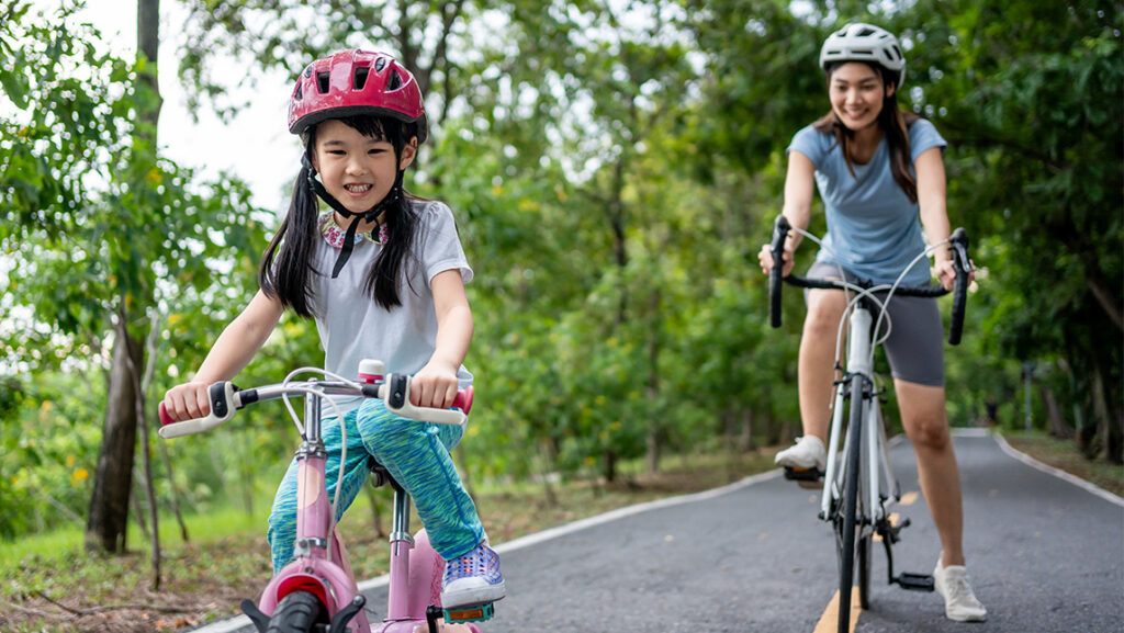 A mother and daughter ride their bikes down a wooded path.