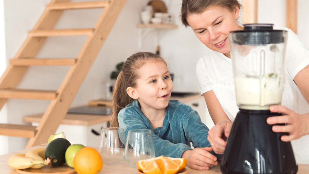 A mom shows her daughter how to make a fruit smoothie.