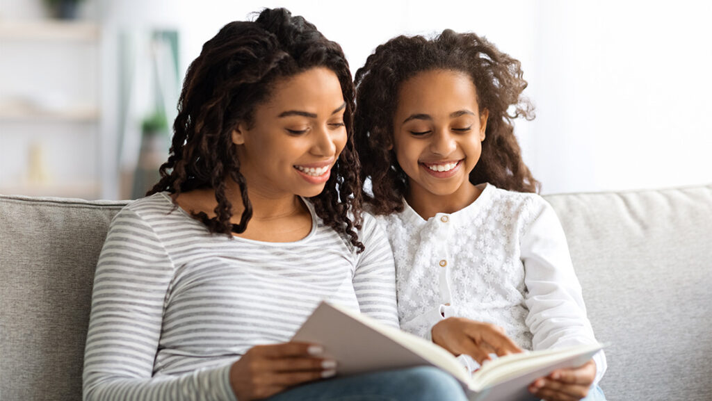 A mother and her pre-teen daughter read a book together.