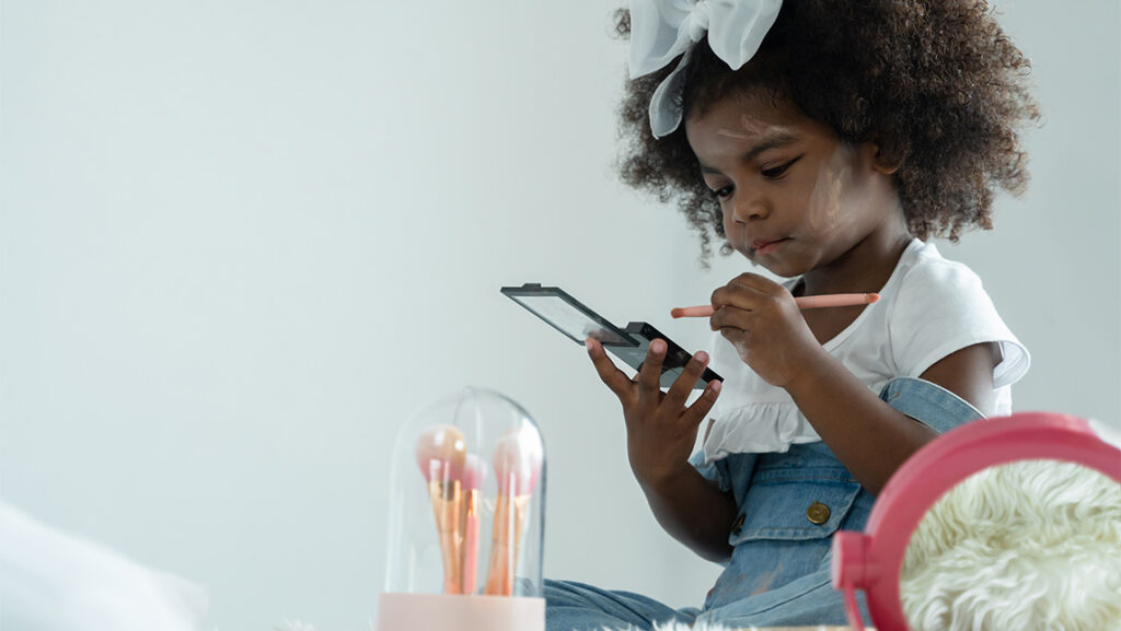 A small girl puts on makeup by herself.