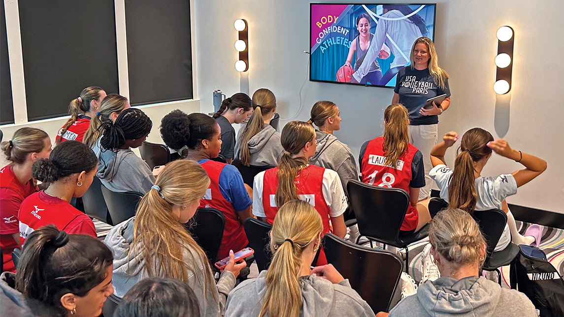 UNCG alumna Jenny Johnson speaks to a large group of young volleyball players.