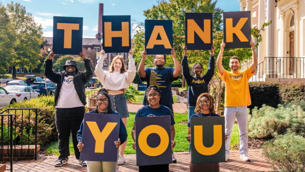 UNCG students each hold a sign with a letter to spell out the word "Thank you."