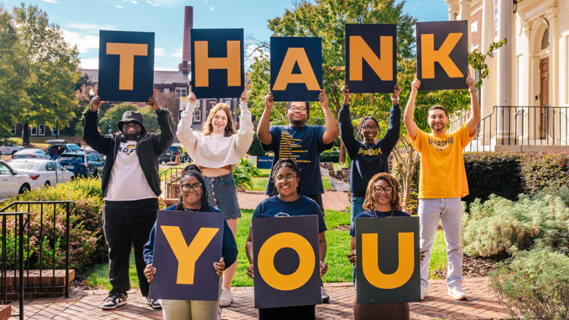 UNCG students each hold a sign with a letter to spell out the word 