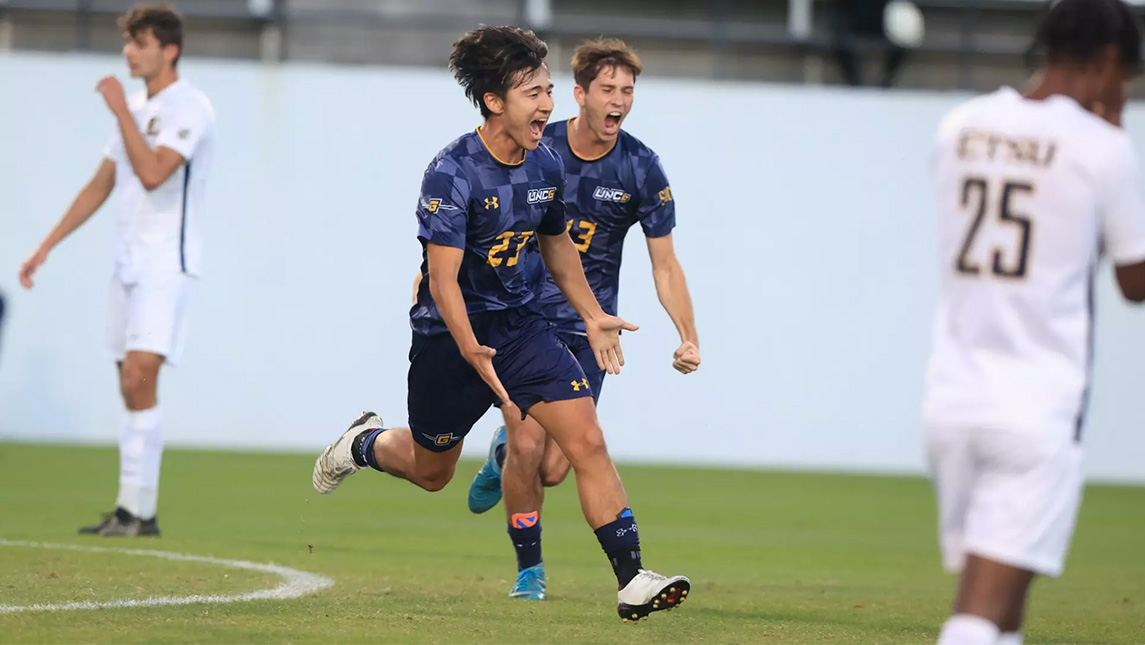 UNCG soccer player Yoshiya Okawa runs across the field in celebration.