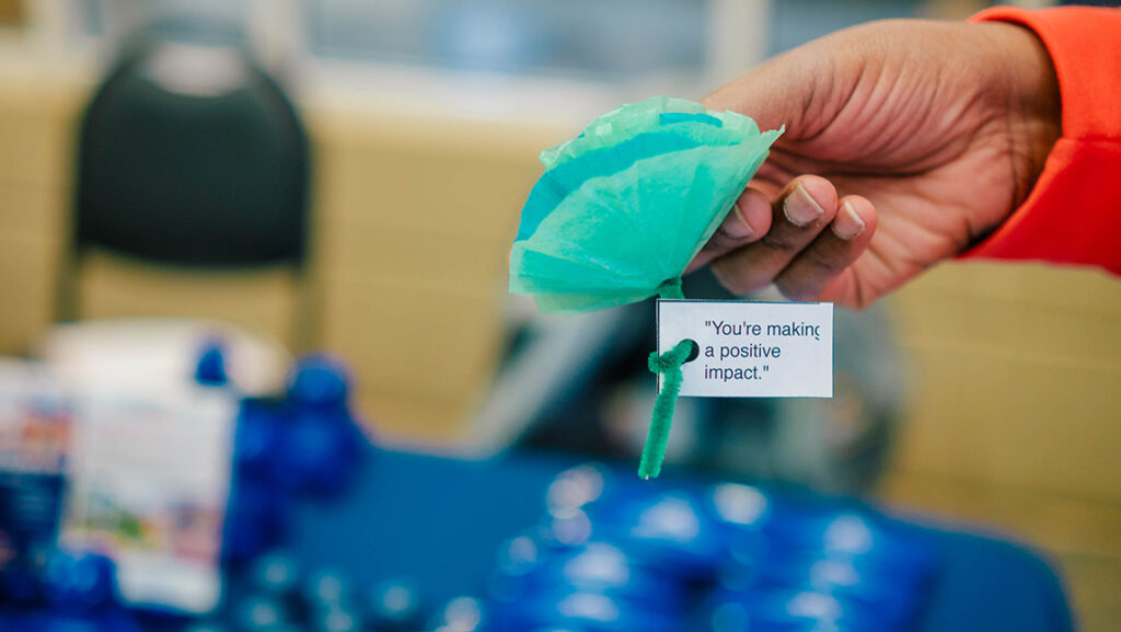 Close-up on someone handing out a tissue paper flower with a positive message tied to its stem.