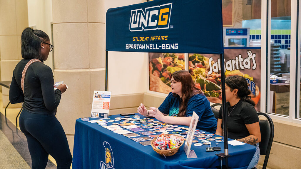 UNCG staff speak to a student at a table promoting wellness.