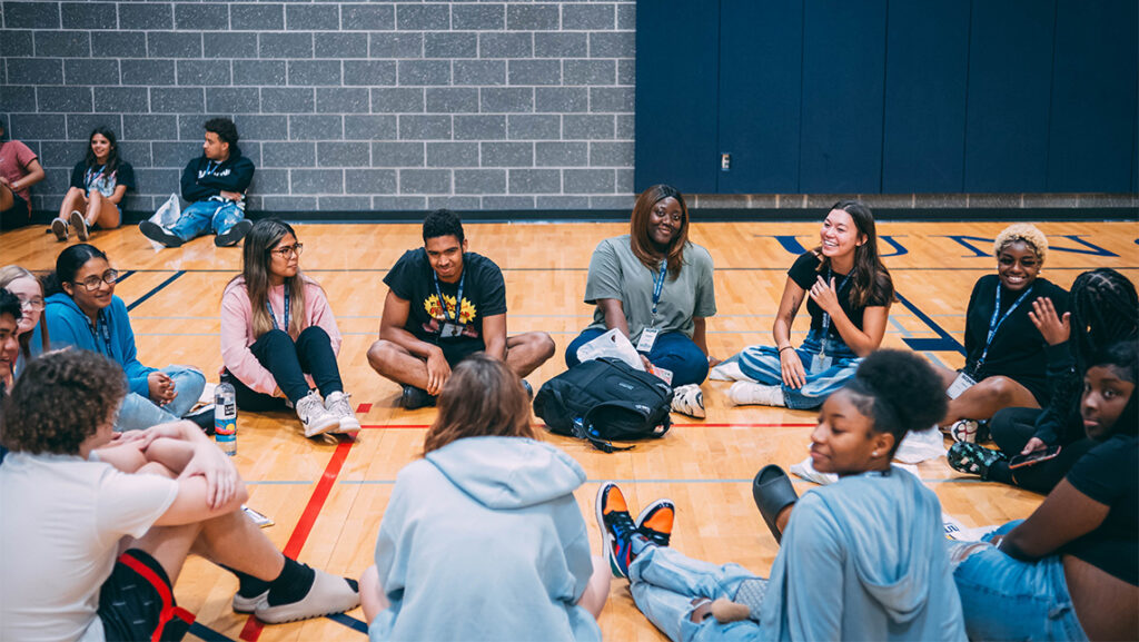 Students sit in a circle of one of UNCG's basketball courts and talk.