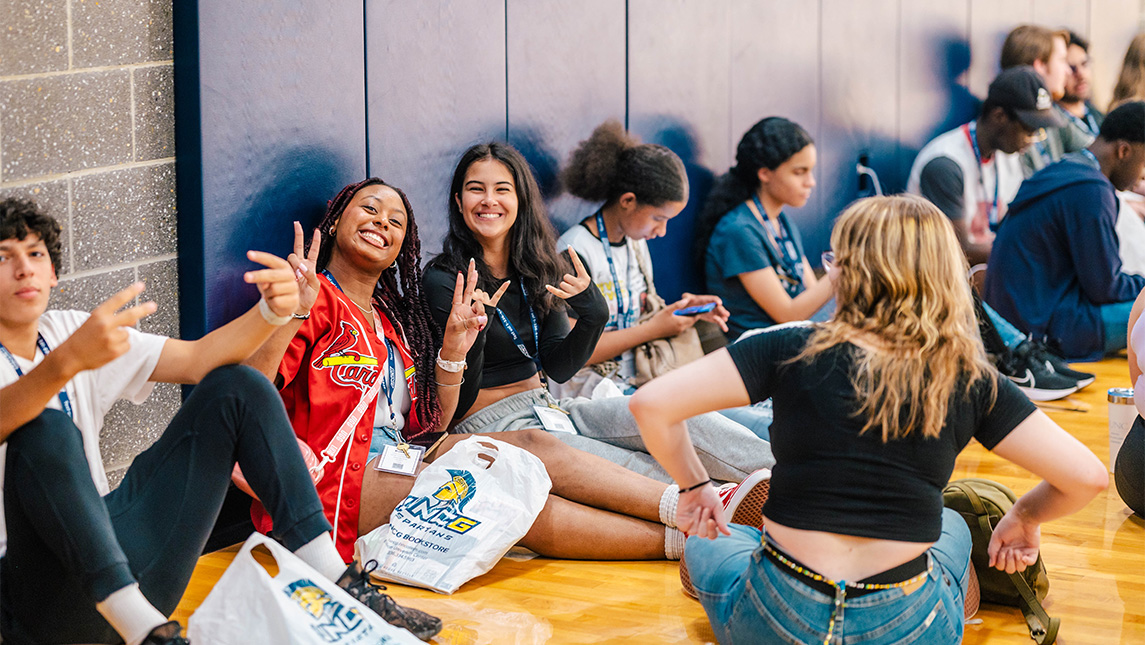 Incoming UNCG students throw up peace signs while sitting Fleming Gym.