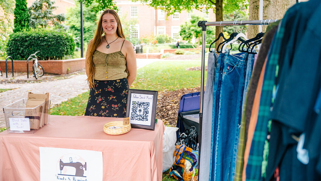 A student entrepreneur at UNCG smiles from her booth full of clothes.