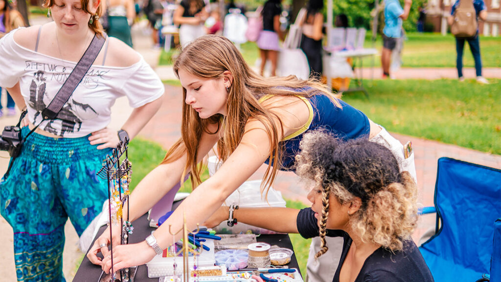 A student business owner adjusts jewelry on a table.