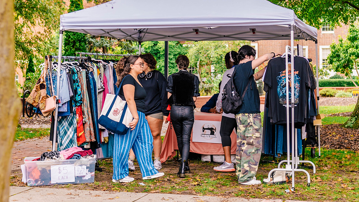 UNCG students look at clothes on racks for sale in an outdoor market.