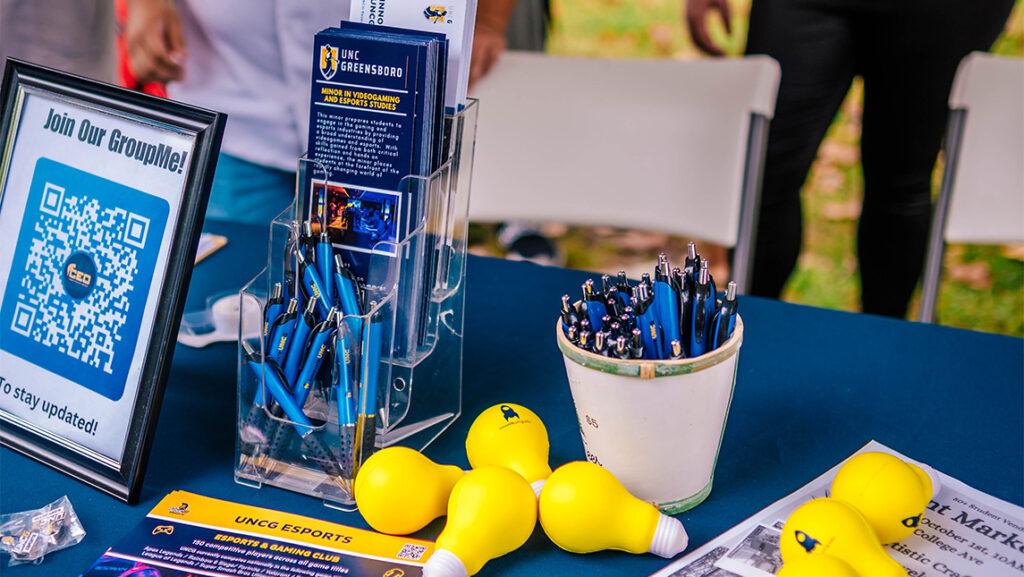 UNCG brochures sit on a table with pens and yellow light bulb ornaments.