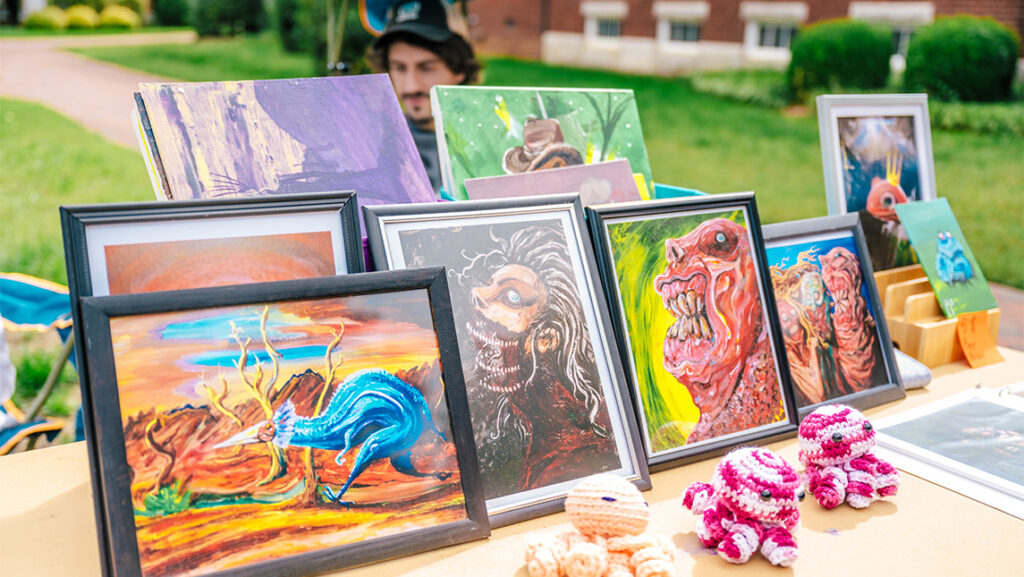 Paintings by a UNCG student sit for sale on a table.